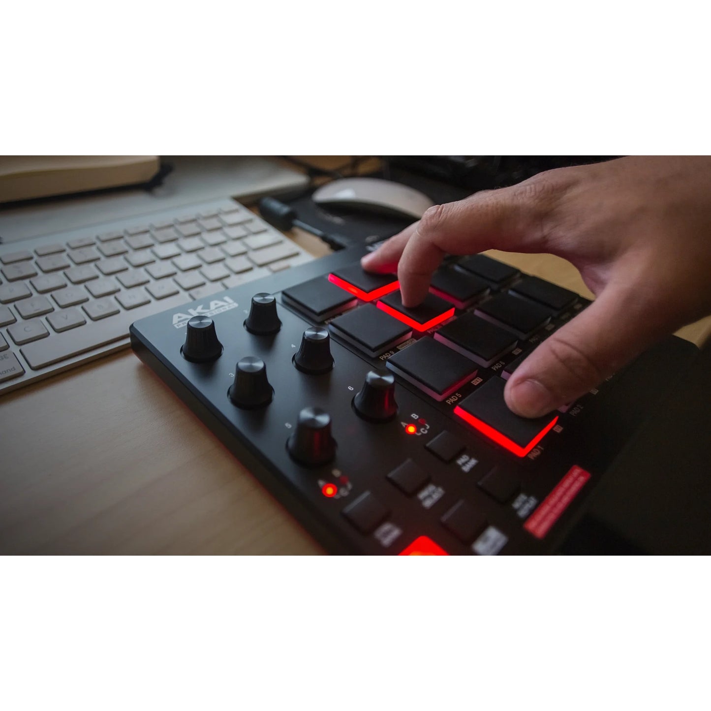 Hand triggering red-lit pads on the Akai MPD218 beside a computer keyboard on a desk