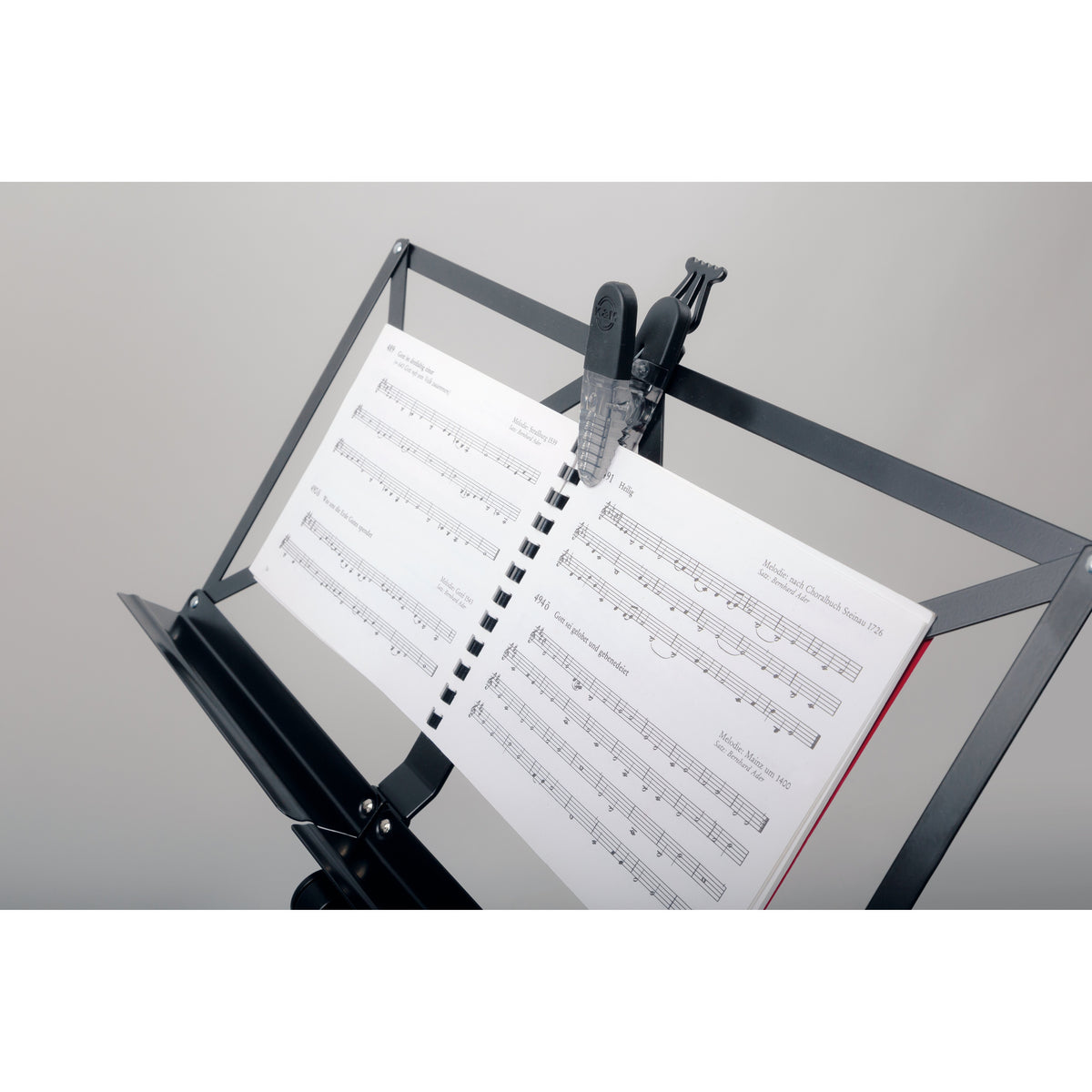 16055 Fix'n Clip in use on a music stand, securing the spiral binding of an open songbook with the clip's magnetic back, K&M