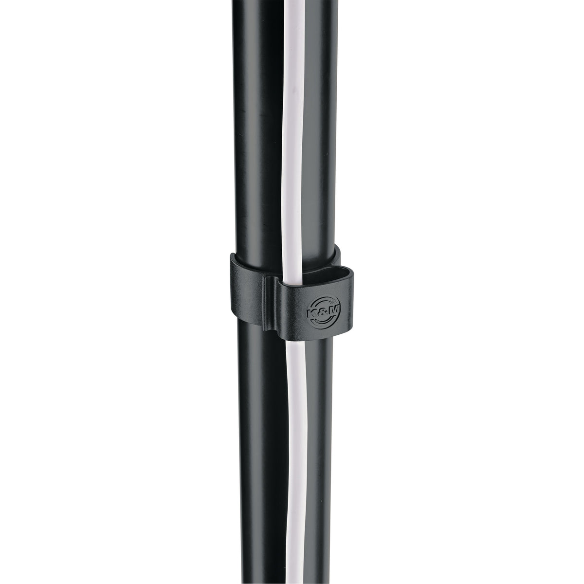 21406 cable clamp in use on black stand tube holding a white cable against the pole, close-up with embossed K&M logo, K&M