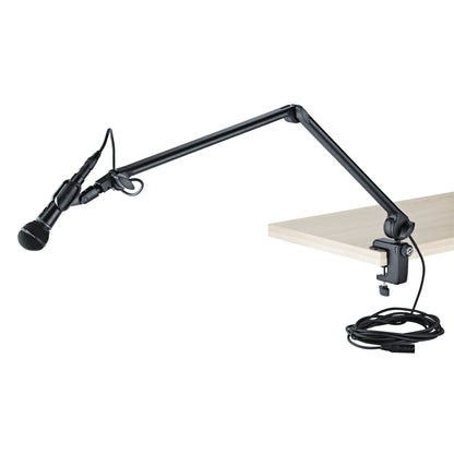 23860 desk microphone boom arm in use clamped to a tabletop holding a handheld dynamic microphone with XLR cable routed along the arm, K&M