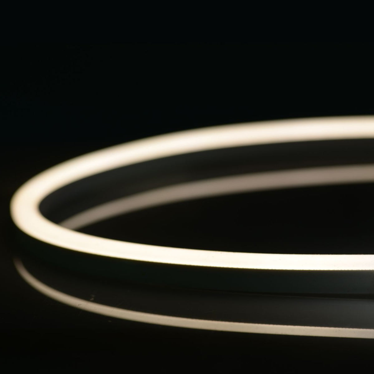 N914-WW-10 QolorFLEX NuNeon warm white LED tape illuminated and coiled on a black reflective surface, City Theatrical