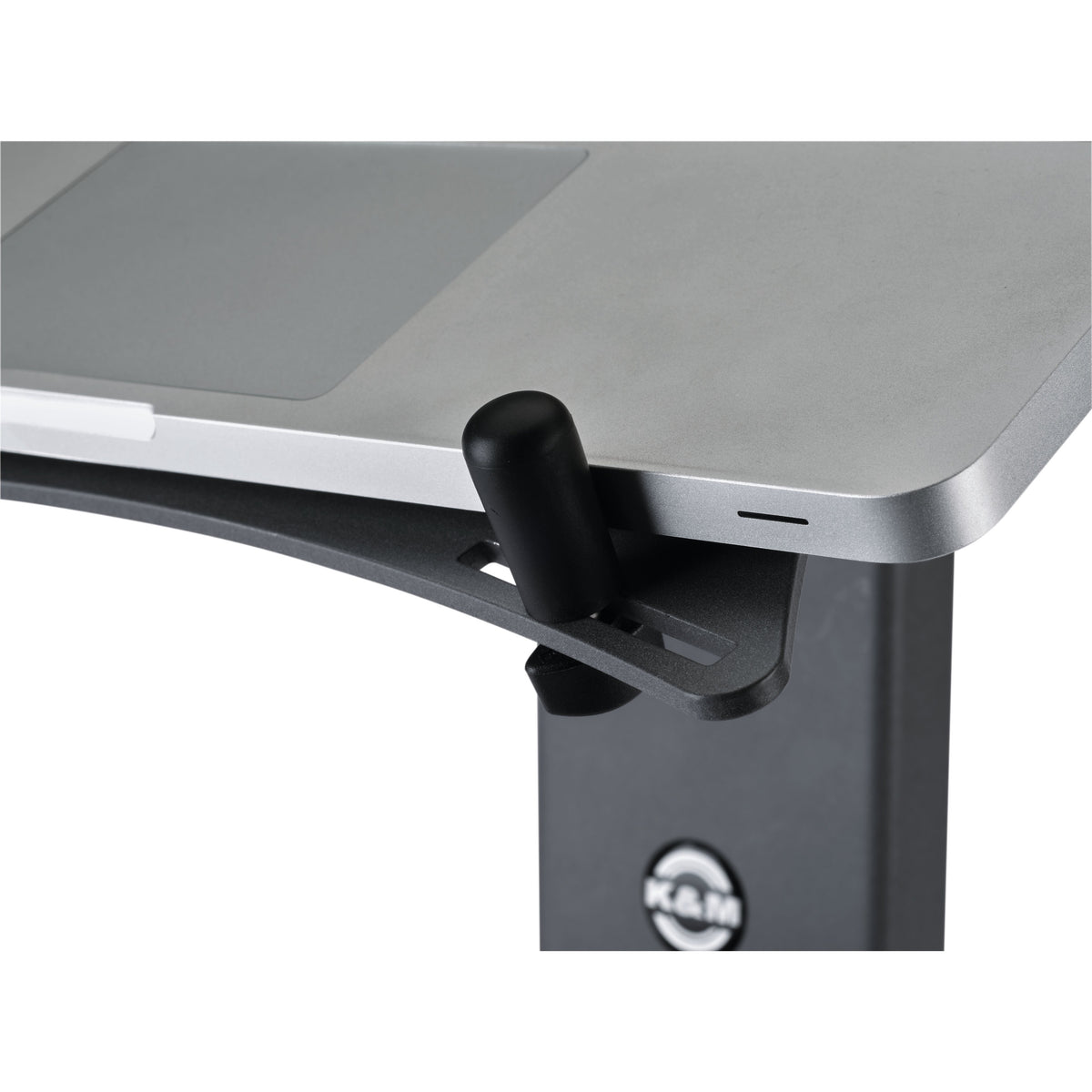 12189 XL stop pin installed in slot of laptop stand shelf holding the edge of a silver laptop, K&M logo visible on stand column, K&M