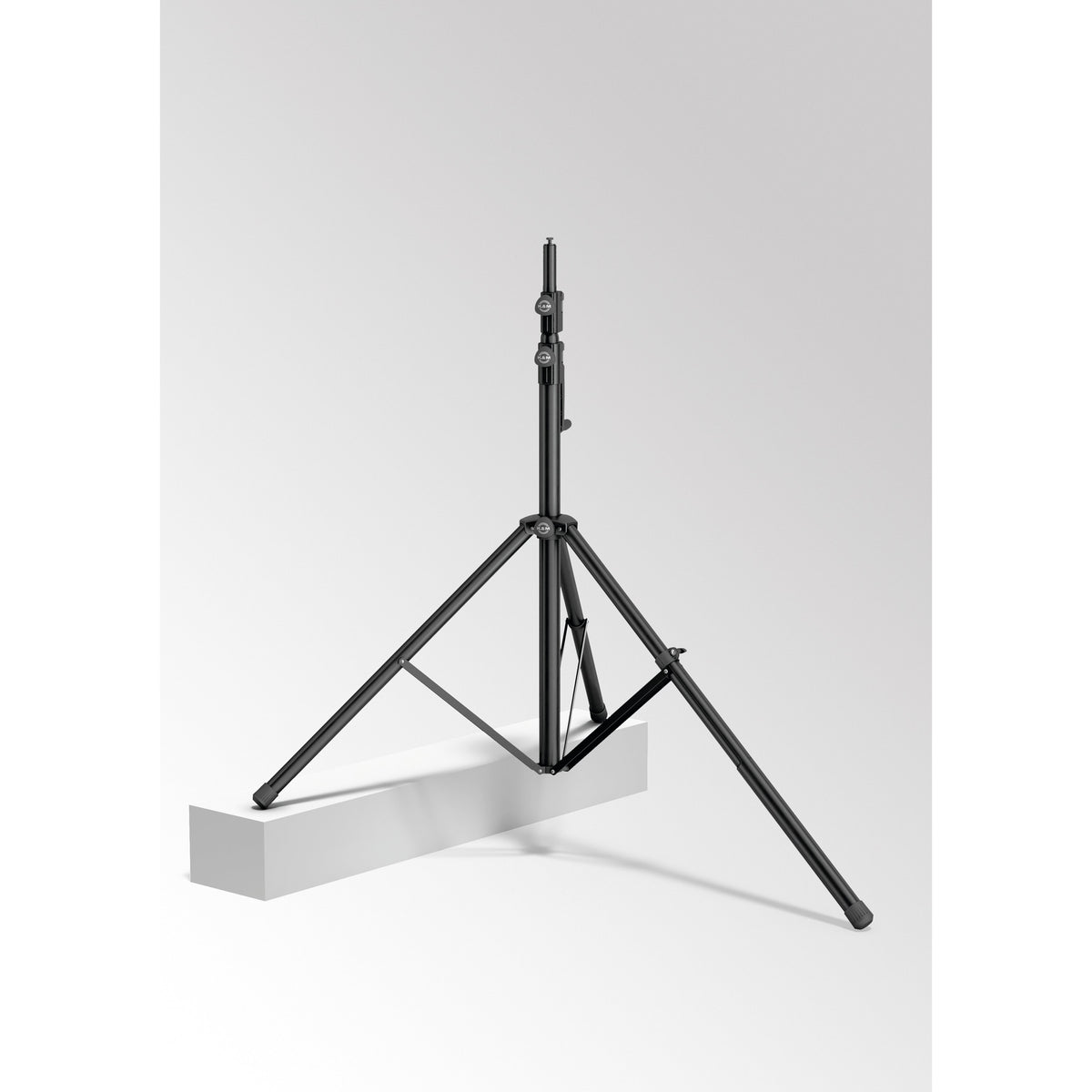 24738 leveling leg in use on a wind-up speaker stand with one tripod leg extended to rest on a raised white block for uneven ground, K&M