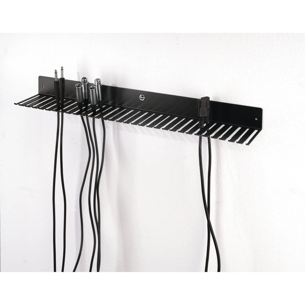 49020 cable hanger mounted on white wall in use, holding TRS jack, XLR and IEC mains cables hanging from the slots, K&M
