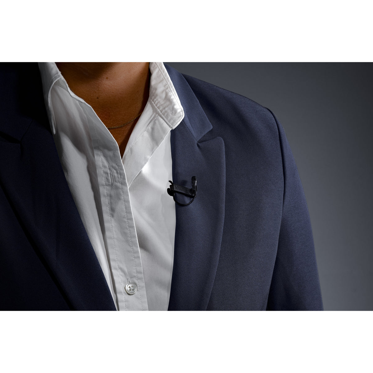 L1 Sonaura lavalier in use clipped to a navy suit lapel with capsule uncovered, Lectrosonics