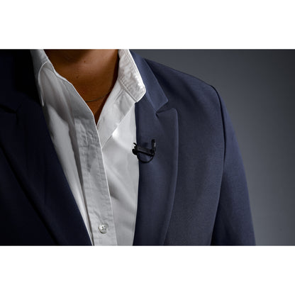 L1 Sonaura lavalier mic in use, clipped to a navy suit lapel over a white shirt with concealed cable, Lectrosonics