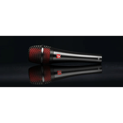 V8 handheld vocal microphone side view lying on a reflective black surface, showing red inner grille mesh, sE logo badge and V8 marking, sE Electronics