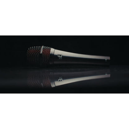 V8 handheld vocal microphone lying on a reflective black surface in a moody studio shot, showing red-lined grille, sE logo and V8 marking, sE Electronics