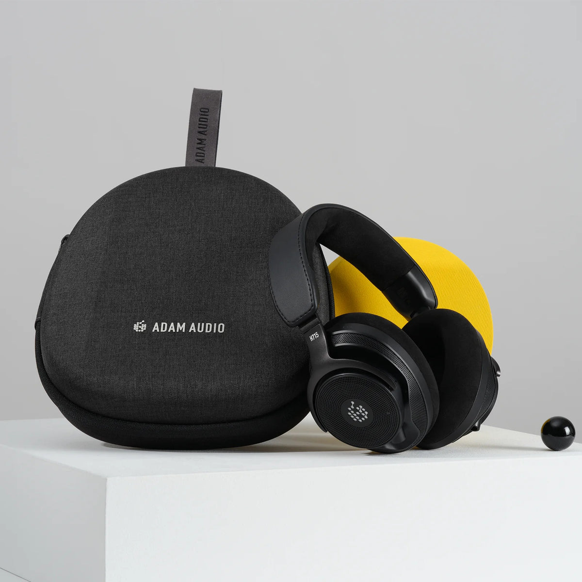 H715 reference headphones displayed beside black fabric carry case with Adam Audio logo and hanging loop, Adam Audio