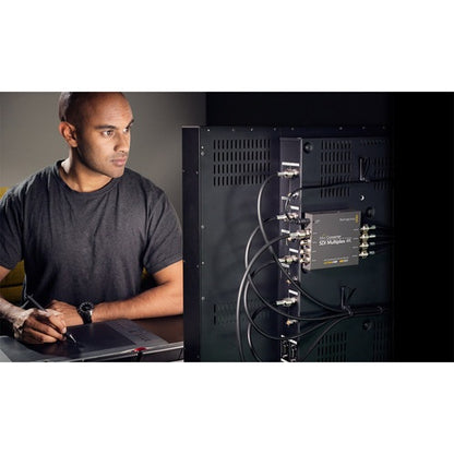 Engineer at a workstation with a Blackmagic Design Mini Converter mounted behind a monitor and BNC cabling