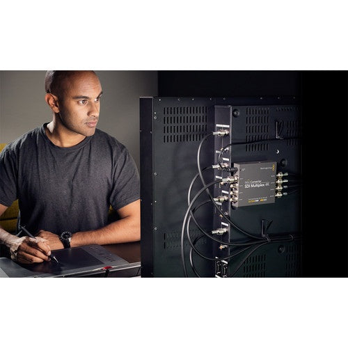 Engineer at a workstation beside a rack with a Blackmagic Design Mini Converter and SDI cabling