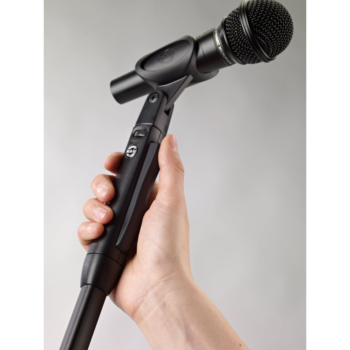 26200 Elegance One-Hand mic stand in use, hand squeezing release grip to adjust height with microphone in clip, K&M