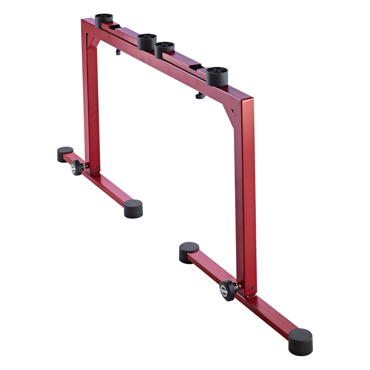 18810 Omega keyboard stand side-angle view in ruby red showing the sliding cross-arms with four black rubber pads and K&M leg knobs, K&M