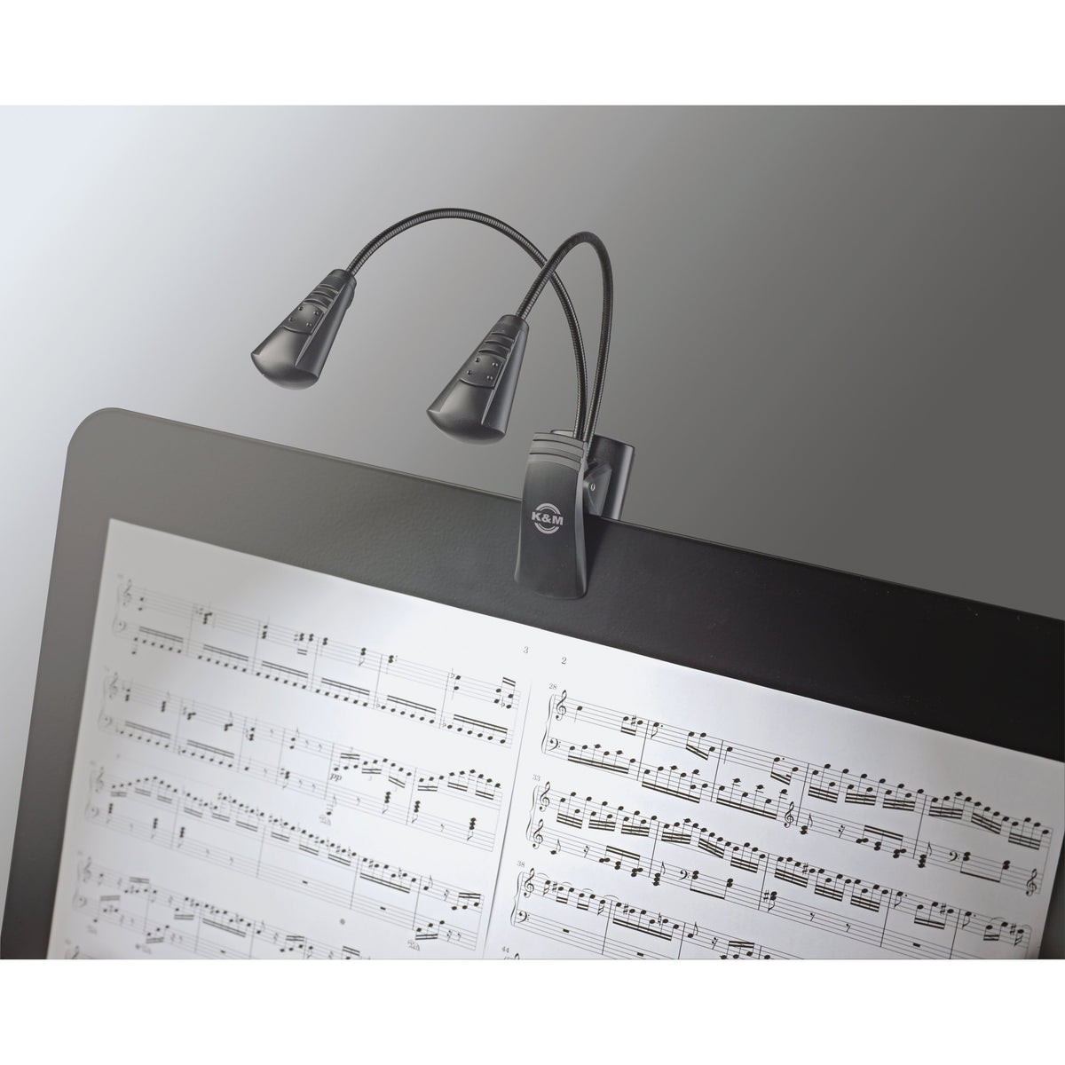 12243 Dual LED FlexLight in use clipped to a music stand desk with both lamp heads angled over open sheet music, K&M