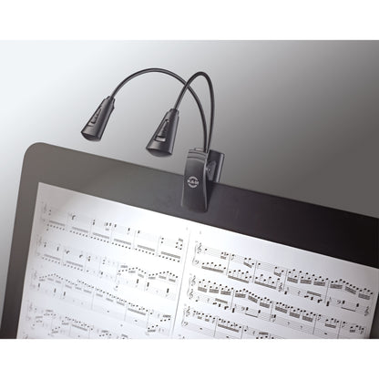 12244 dual-head LED FlexLight in use clipped to a music stand, lamp heads angled to illuminate open sheet music, K&M