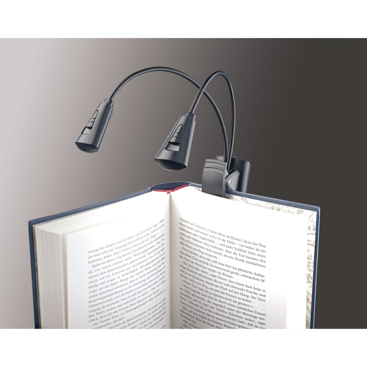 12244 dual-head LED FlexLight clipped to the cover of an open book, showing lamp head slide switches and goosenecks, K&M