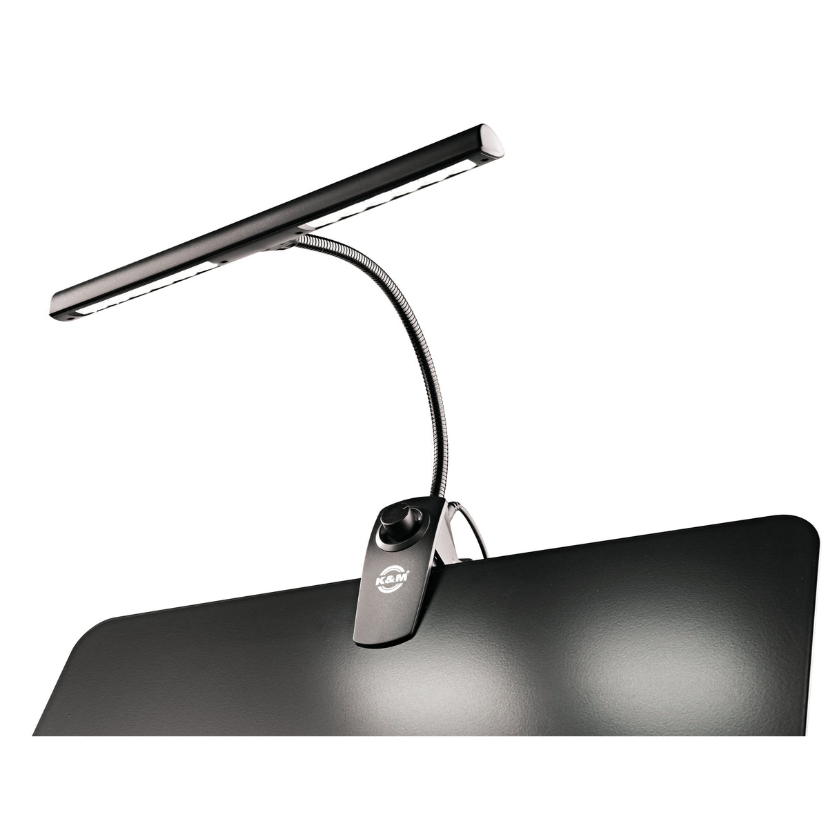12295 music stand light mounted on a black music desk with LED bar switched on and light pooling across the desk surface, K&M