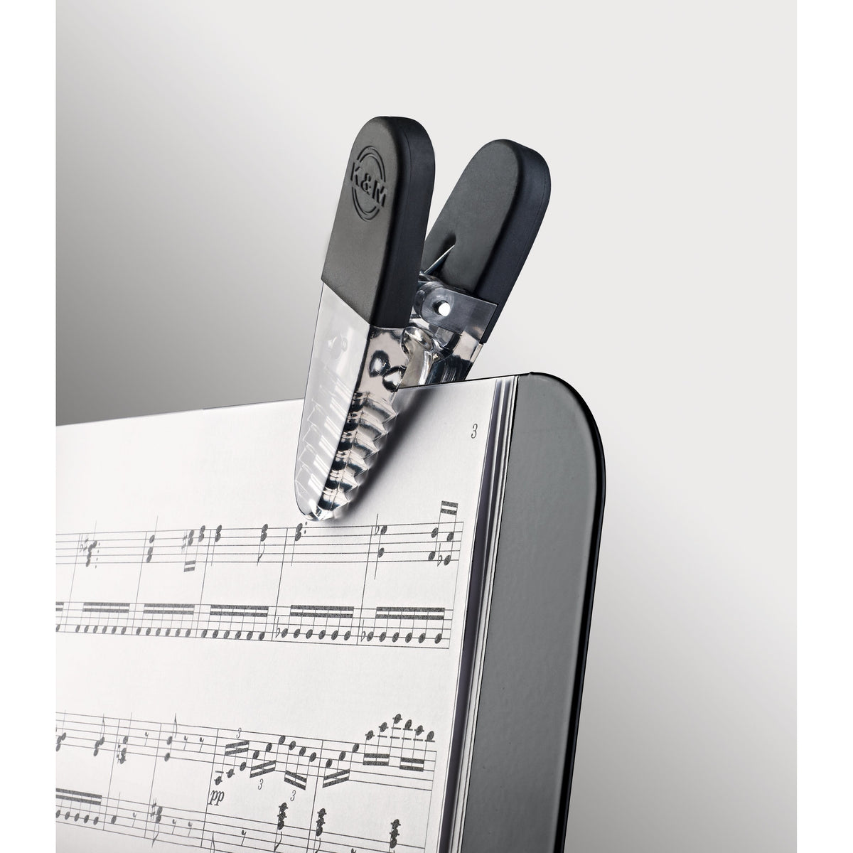 16055 Fix'n Clip close-up detail of black clip with embossed K&M logo and clear ribbed jaw holding sheet music pages, K&M