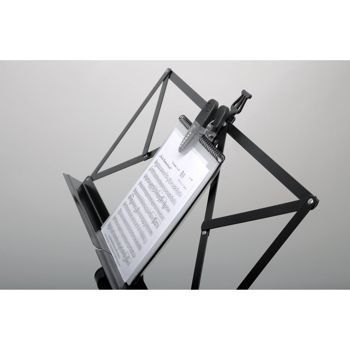 16055 Fix'n Clip in use on a folding black music stand, holding a spiral-bound score upright at the top edge, K&M