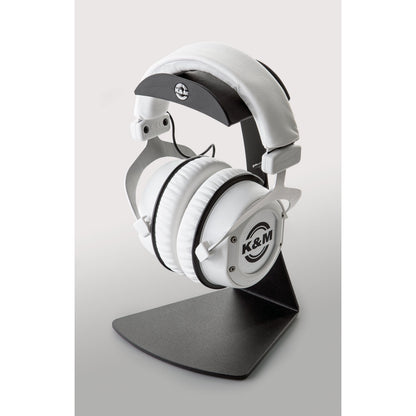 16075 headphone table stand in use with white over-ear headphones resting on the padded headband cradle, K&M logo visible on the cradle, K&M