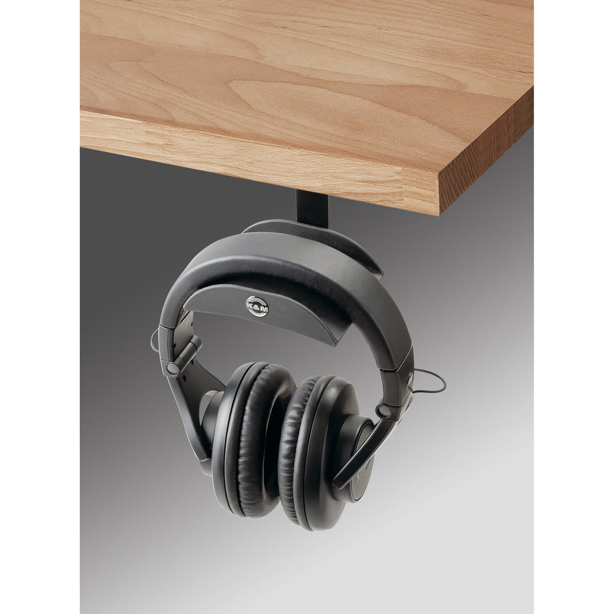 16330 headphone holder mounted under a wooden table edge with studio headphones hanging from the curved rubber support, K&M