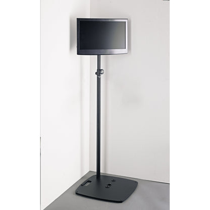 19610 stand adapter in use holding a flat-screen monitor on a black extension tube and weighted floor base in a room corner, K&M