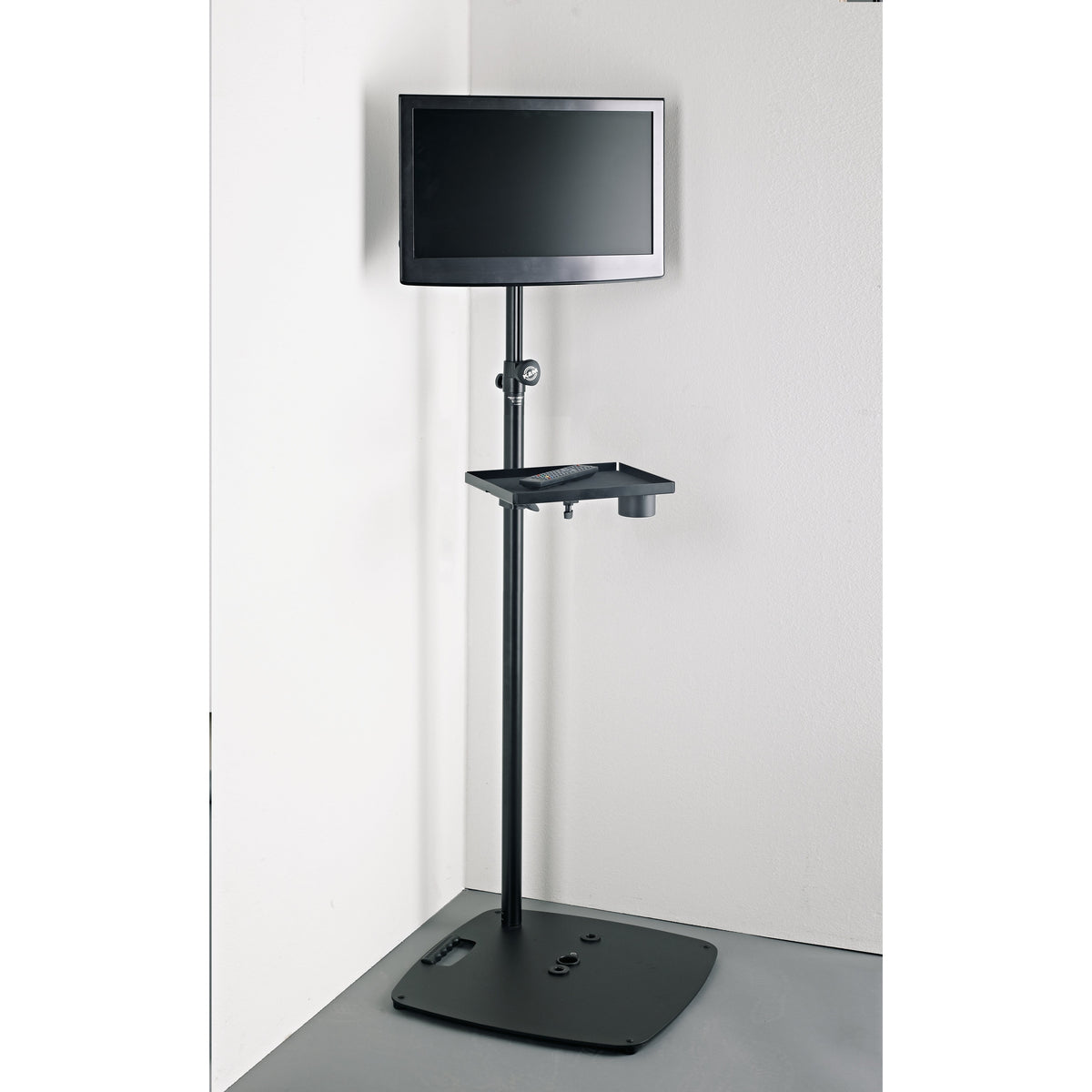 19610 stand adapter in use with monitor on a floor stand and an accessory tray holding a remote control and cup holder, K&M