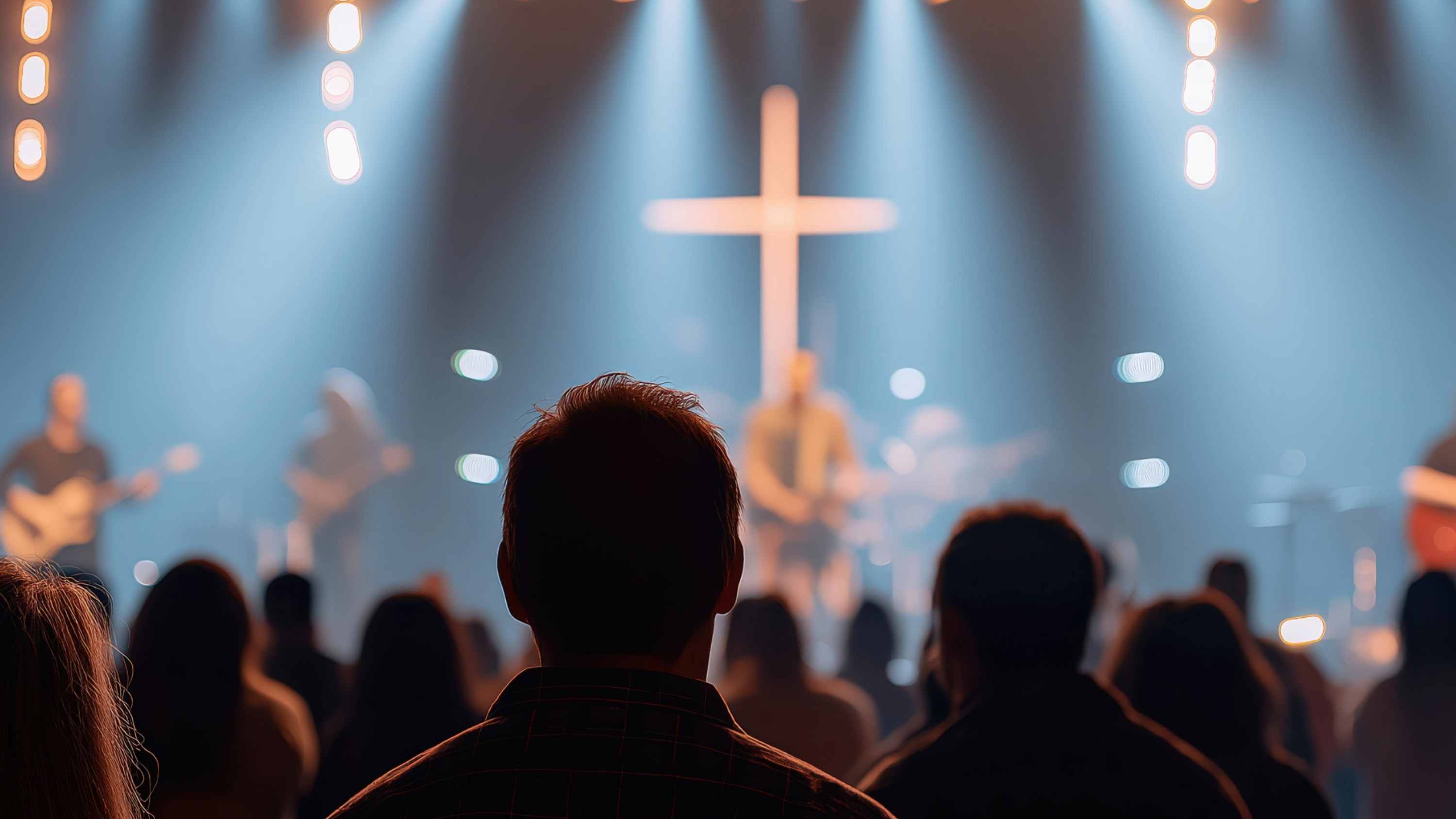 People in a church auditorium with a cross on the stage, illuminated by stage lights.