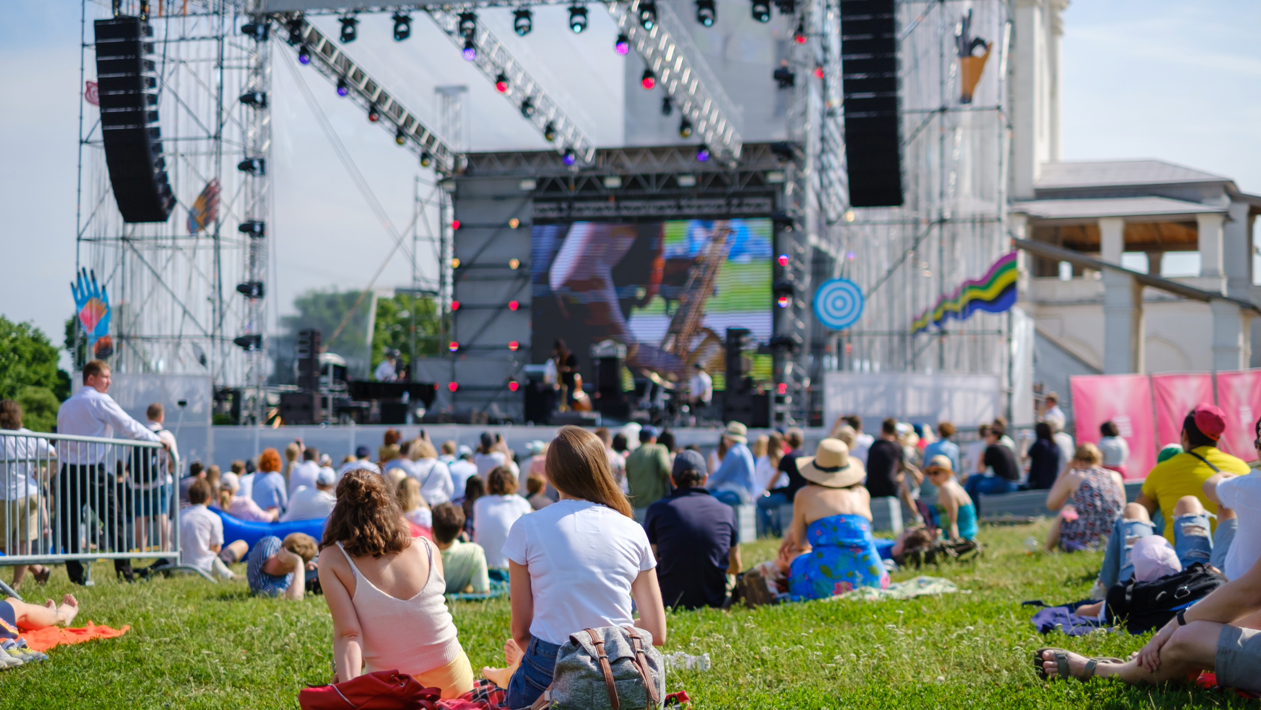 People at an outdoor concert with a stage and large screen displaying a performance.